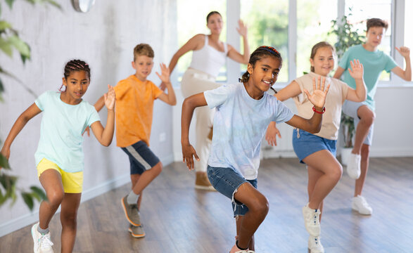 Positive African male child dances vogue in choreographic school. Group of young people in sportswear trains together with classmates in gym before competitions, teacher take part in class background - Powered by Adobe