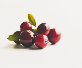 A cluster of fresh red cranberries with green leaves is arranged artistically on a light background, highlighting their vibrant color and natural beauty, perfect for culinary presentations