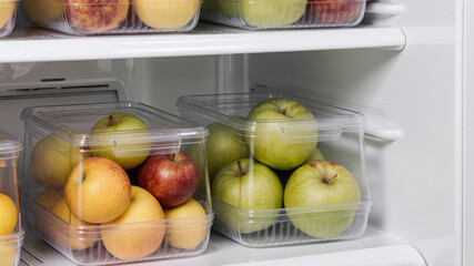Transparent fridge bins storing apples and green peppers placed on lower refrigerator shelf