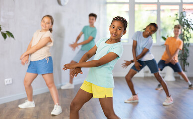 Obraz premium African positive girl dances waacking in choreographic school, group of young people in sportswear trains together with their classmates in gym before competitions, battle