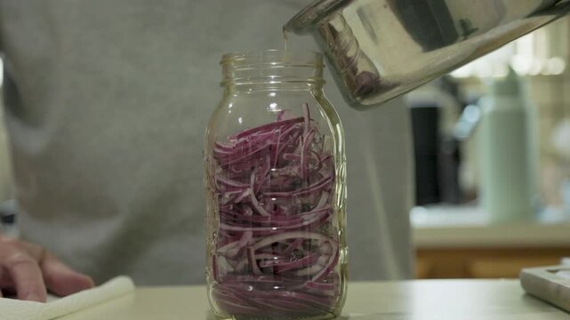 pouring vinegar mixture over onions in a jar