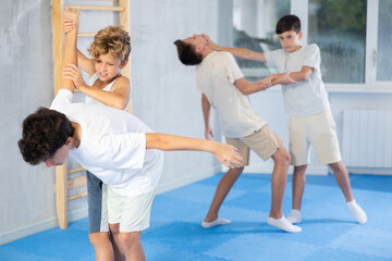 Willing junior attendee of self-defense classes practicing arm twist on a standing boy in sports...