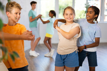African boy and light-skinned girl dance in pairs and rehearse jive dance before performing on main floor. Classes for children workout in mini group gym.