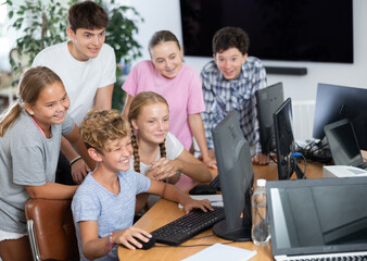 Curious underage boys and girls looking at monitor of computer together with trainer during IT...