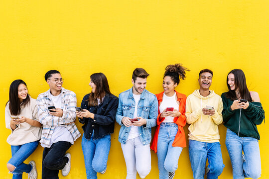 Young group of people having fun using mobile phone over yellow wall. Communication and social media concept