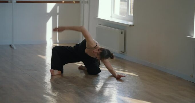 Young woman in black suit performs smooth and graceful movements during her contemporary parter choreography in dance studio
