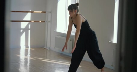 Side view of athletic girl in black suit performing stretching and dance preparation moves during her contemporary dance rehearsal in small bright studio - Powered by Adobe