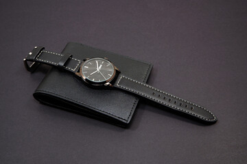Black leather watch on black wallet with black background close-up view