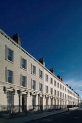 Obraz premium Neatly arranged rows of charming white townhouses gracefully line the street, creating a picturesque scene beneath a vast and vibrant deep blue sky on a beautiful clear afternoon