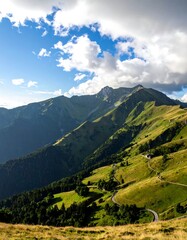 Fototapeta premium A picturesque vista of rolling hills and mountains under a vibrant blue sky, dotted with fluffy white clouds, showcasing a winding road snaking through the landscape.