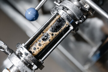 Close-up of beer brewing process with stainless steel equipment and foamy liquid in brewery