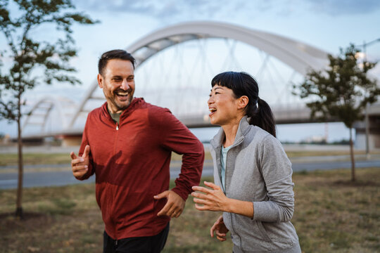 Happy couple running and smiling near bridge in urban setting