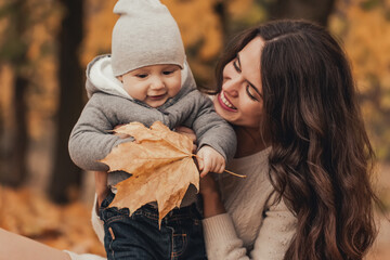 Young and happy mom dressed in cozy knitted clothes walking and having fun with her little son in...