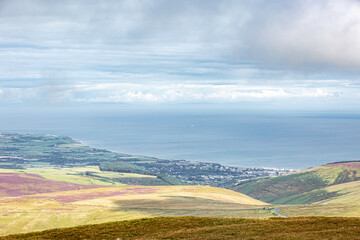 Fototapeta premium Laxey, Isle of Man 08,05,2023 Beautiful view of the ocean and a town in the distance. The sky is cloudy and the water is calm Isle of Man -