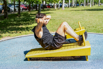 Side view of a young man doing sit-ups on outdoor fitness equipment