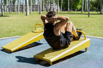 Young man doing sit-ups on outdoor fitness equipment