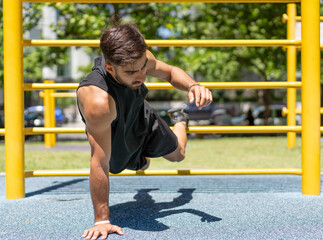 Young man doing one-handed push-ups on outdoor fitness equipment