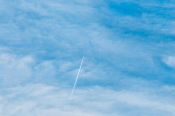 Trace of a flying airplane in the blue sky with soft white fluffy clouds background