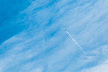 Trace of a flying airplane in the blue sky with soft white fluffy clouds background