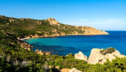 Coastal view of a Mediterranean bay. Lush greenery hugs rocky cliffs, meeting a turquoise bay.  Clear blue sky