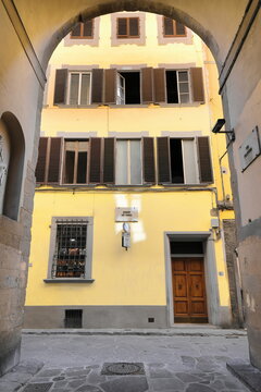 The arch at Via Filippina Street south end frames the simple facade of a three-story yellow building with brown window shutters. Florence-Tuscany-305