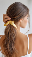 Naklejka premium Elegant hair styling: woman brushing long hair with gold ribbon for glamorous look