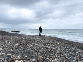 Stormy day at the beach after the rain. A person standing far off, looking at the clouds and the ocean. Silhouetted person.