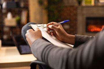 Black male psychologist writing in notepad, taking notes at private clinic. African american therapist with pen in hand, documenting on clipboard during session in brick wall office.