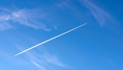 A wispy, white contrail stretches across a vibrant, cerulean sky, dotted with delicate clouds.