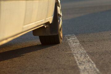 A car tire is positioned strategically near a distinct white line on an asphalt road, effectively demonstrating the importance of road positioning and clear roadway markings for safety