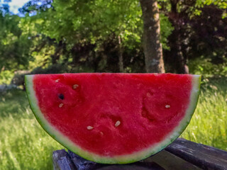 a fresh, juicy slice of watermelon with visible seeds, vibrant red flesh, and a green rind, placed on a rustic wooden surface, perfect for a refreshing summer snack