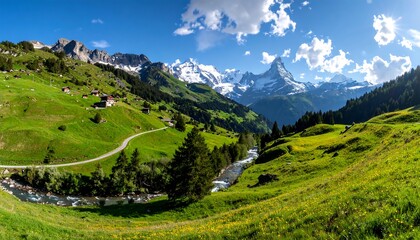 Naklejka premium A picturesque valley unfolds with lush green meadows, winding roads, and towering snow-capped mountains under a vibrant blue sky.