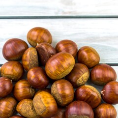 Obraz premium Pile of brown chestnuts on a light wooden surface
