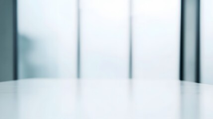 A simple, clean, and modern interior scene, featuring a smooth, white table surface in front of a blurred window.