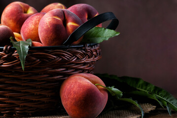 Still life of a brown woven basket fillled with fesh picked yellow peaches with a mottled background with copy space.