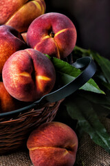 Vertical closeup of fresh picked yellow peaches in a basket with leaves.
