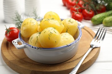 Tasty young boiled potatoes with dill in bowl and fork on white wooden table, closeup