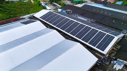 An aerial view of technicians installing a solar panel farm on a warehouse roof. This is a...