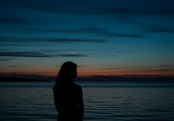 Silhouette of a woman standing by the sea at dusk looking at the horizon