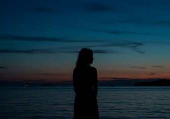 Silhouette of a woman standing by the sea at dusk looking at the horizon