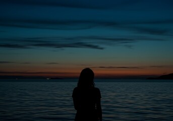 Silhouette of a woman standing by the sea at dusk looking at the horizon