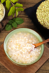 Rice porridge with buckwheat grains on wooden table - healthy breakfast bowl with fresh herbs
