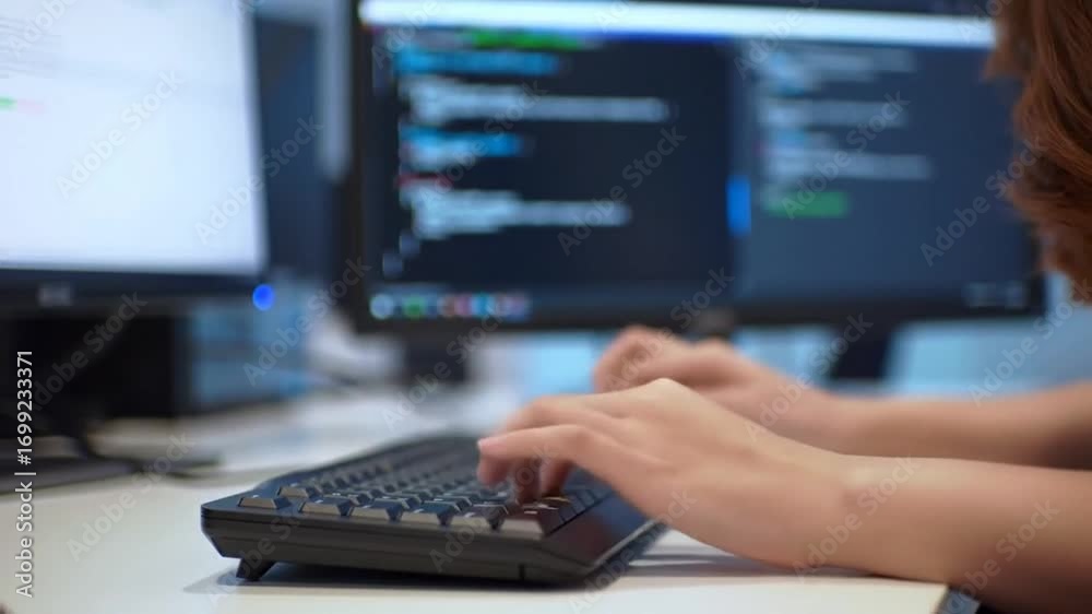 Wall mural person diligently coding, hands actively typing on keyboard, focused on dual computer screens displa