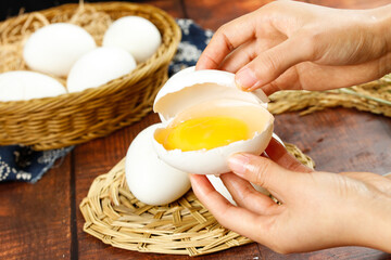 Fresh Goose Eggs in Wicker Basket with Hands Cracking Open Egg Showing Golden Yolk