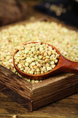 Raw buckwheat grains in wooden spoon on rustic wood background - healthy whole grain cereal ingredient
