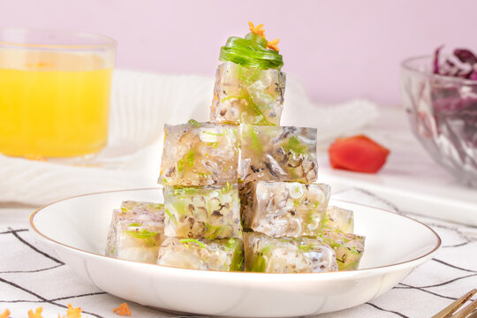 Fish aspic jelly cubes with herbs in translucent gelatin on white plate - traditional appetizer dish