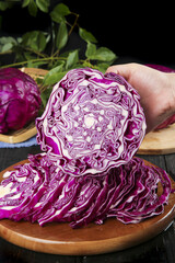 Obraz premium Hand Slicing Fresh Purple Cabbage on Wooden Cutting Board Showing Vibrant Cross-Section and Leafy Texture