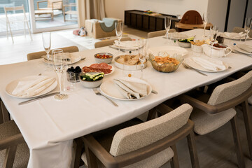 Elegant dining table set for celebration with appetizers, bread, cured meats, vegetables, and champagne glasses in a modern home interior, ready for family gathering or festive dinner.