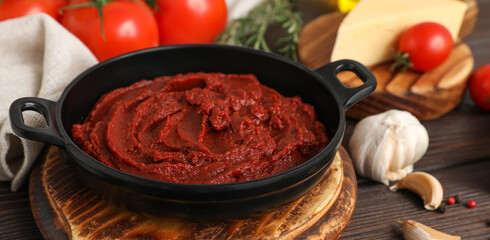Frying pan with tomato paste on dark wooden background, closeup