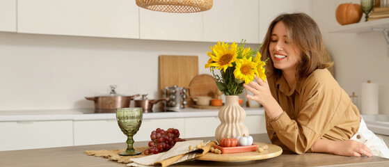 Pretty young woman with autumn flowers, grapes and pumpkins in kitchen